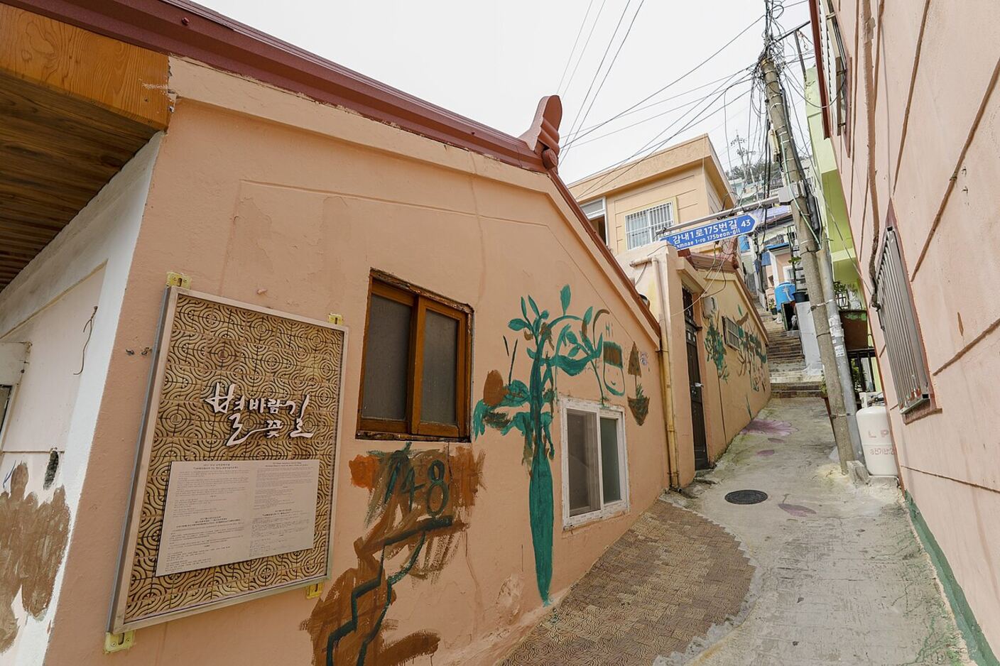 A narrow painted alley in Gamcheon between houses, with a mural on the wall and steps climbing away at the end