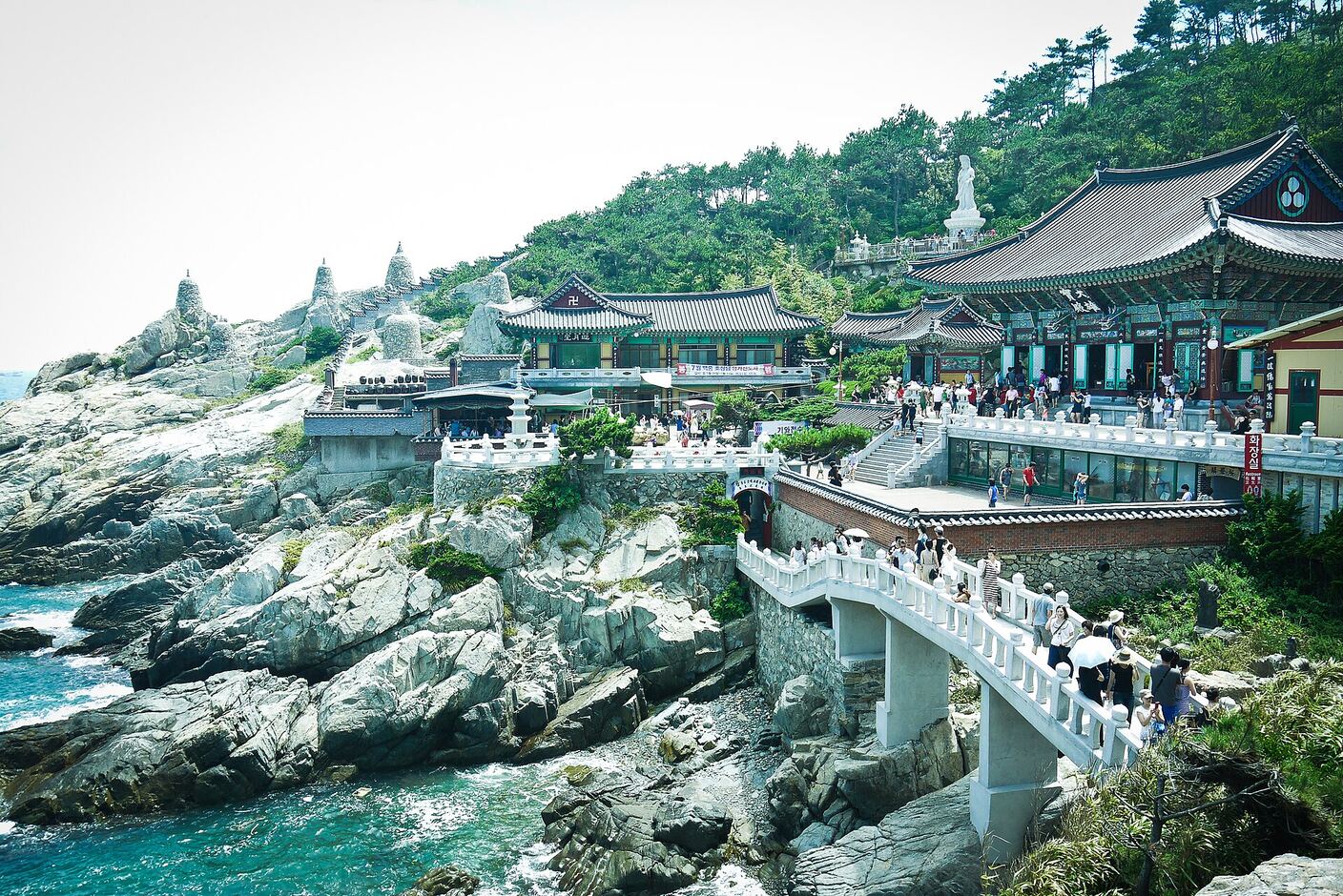 The white stone bridge crossing to the main precinct of Haedong Yonggungsa, shrine halls on the rocks above and the sea below