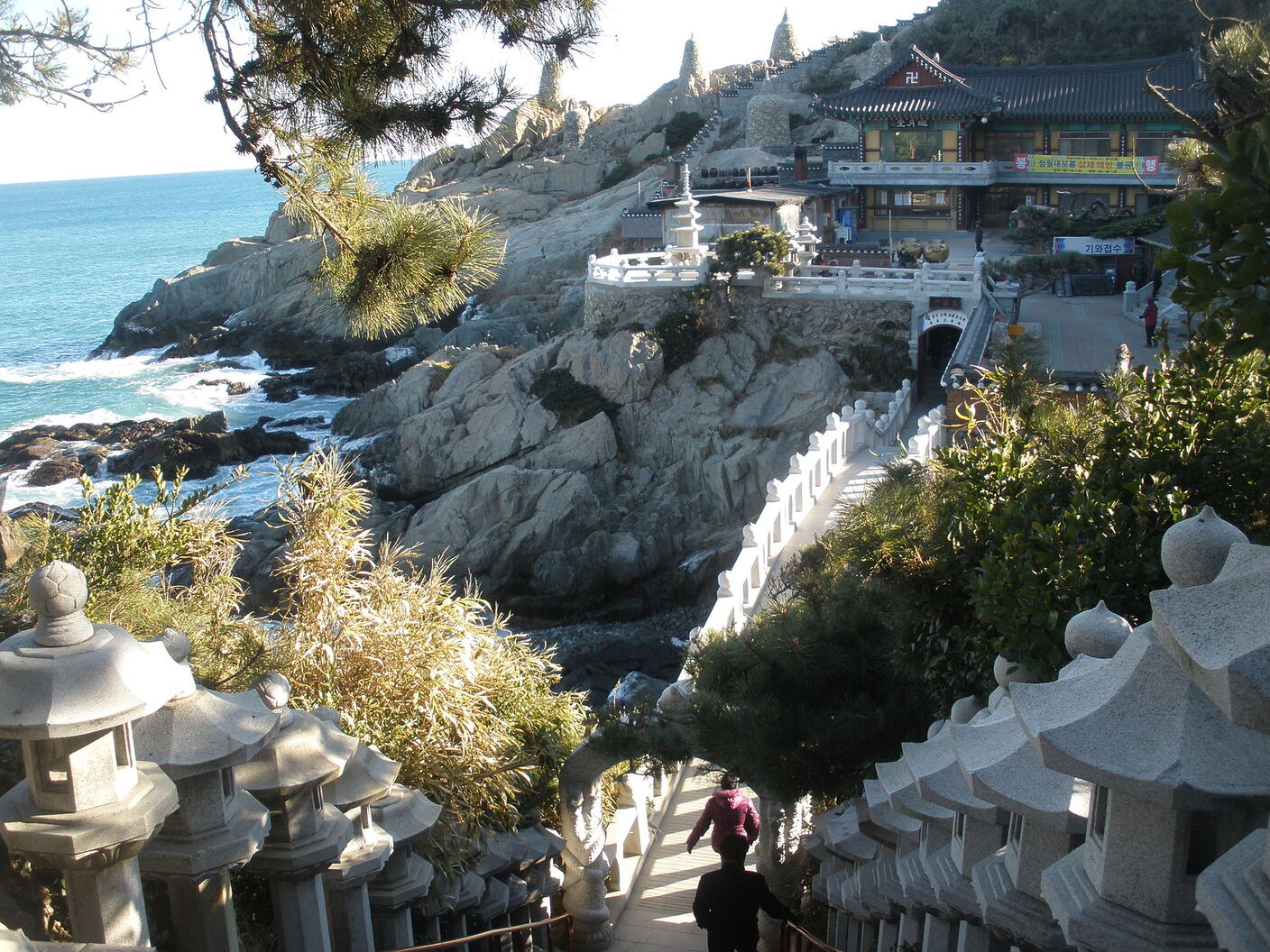 Stone lanterns lining the stepped path down to Haedong Yonggungsa, with the bridge and the sea below