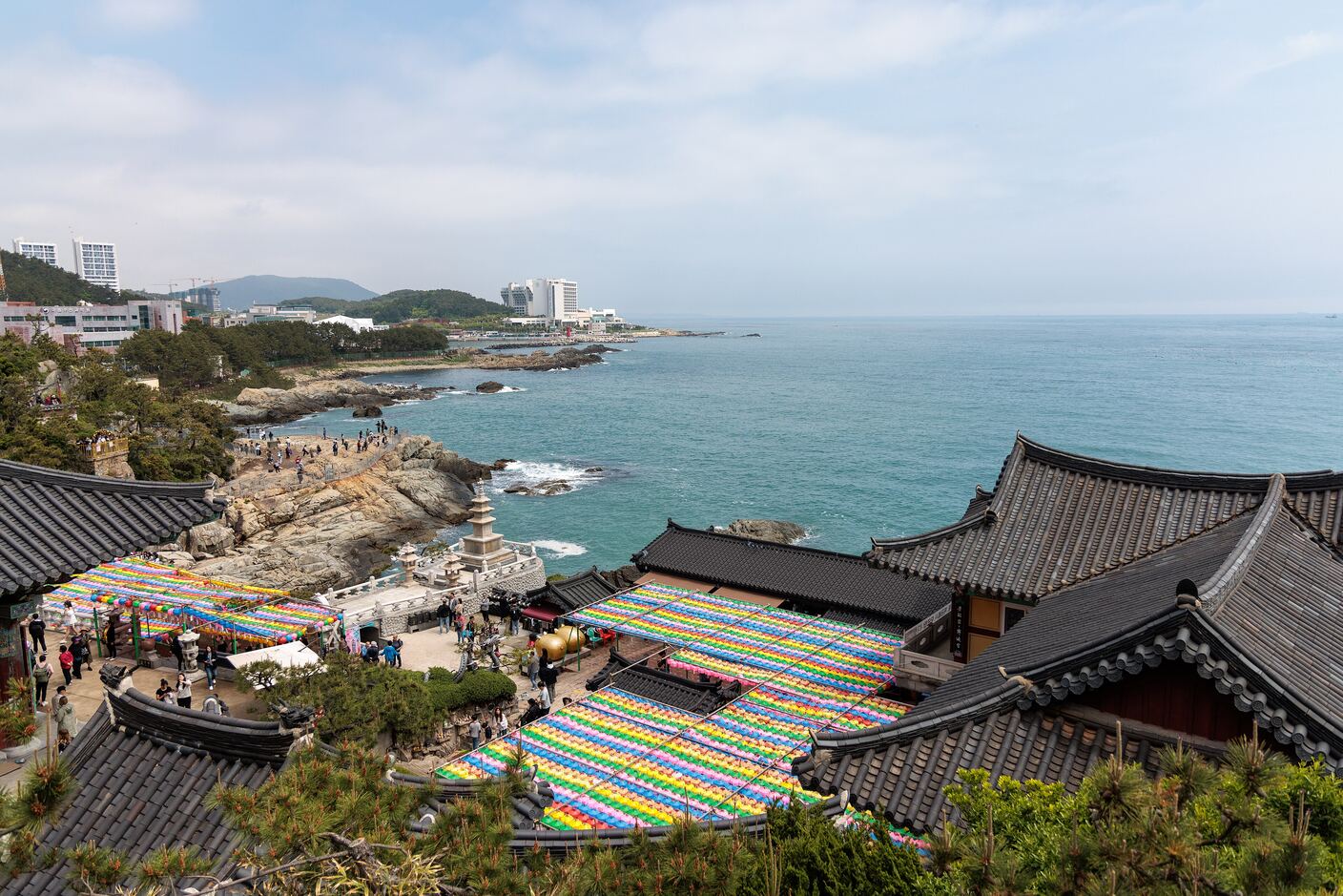 Rows of coloured paper lanterns strung above the courtyards of Haedong Yonggungsa for Buddha's Birthday, with the coastline beyond