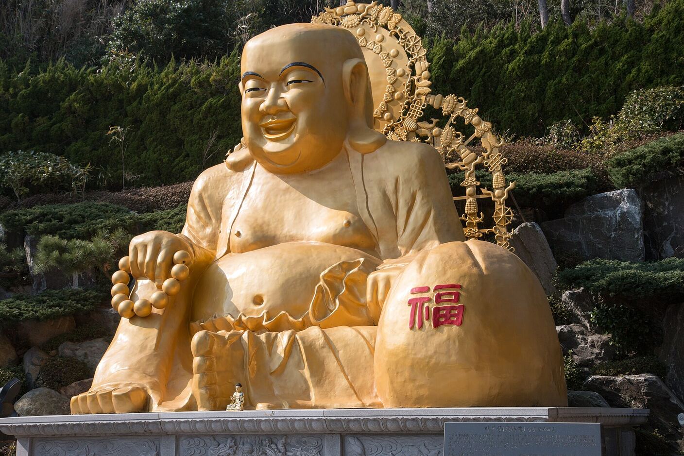 A large gilded seated Maitreya Buddha at Haedong Yonggungsa, smiling, with a red good-fortune character on the sack at his side