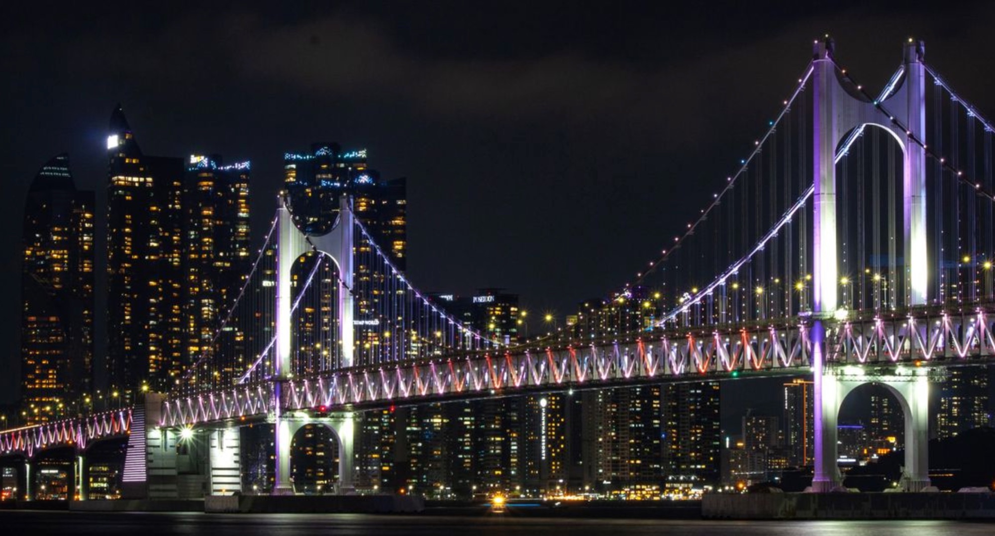 Gwangan Bridge lit in colour over the water at night in Busan